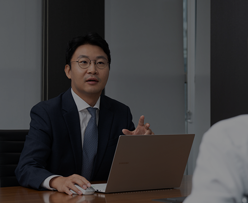 노트북 앞에서 말하며 손짓하는 정장 차림 사람